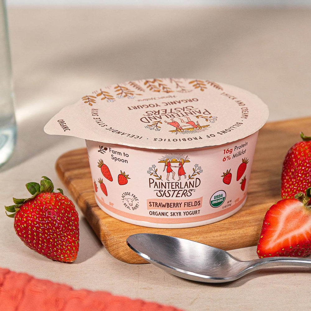 Painterland Sisters Strawberry Fields organic skyr yogurt cup on cutting board next to spoon and sliced strawberries
